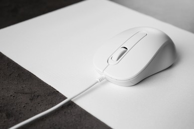 Photo of Wired mouse with mousepad on black textured table, closeup