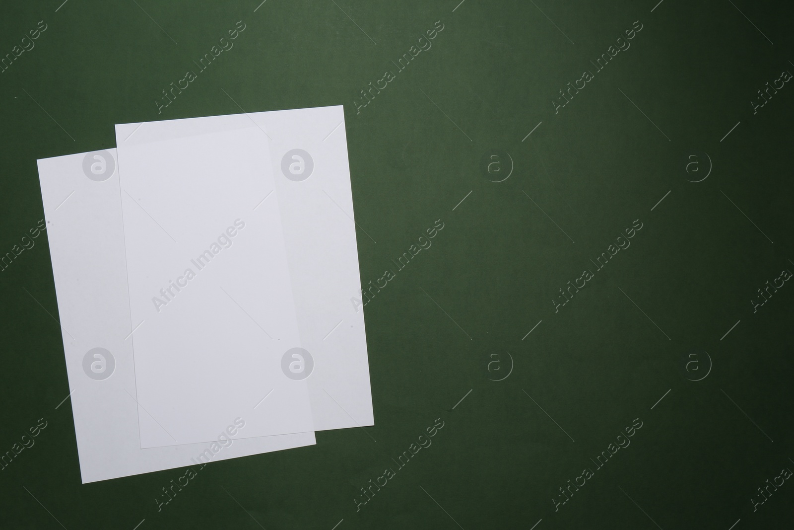 Photo of White paper sheets on dark green background, top view. Space for text