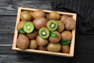 Crate with cut and whole fresh kiwis on black wooden table, top view