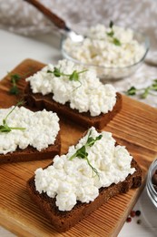 Bread with cottage cheese and microgreens on wooden board, closeup