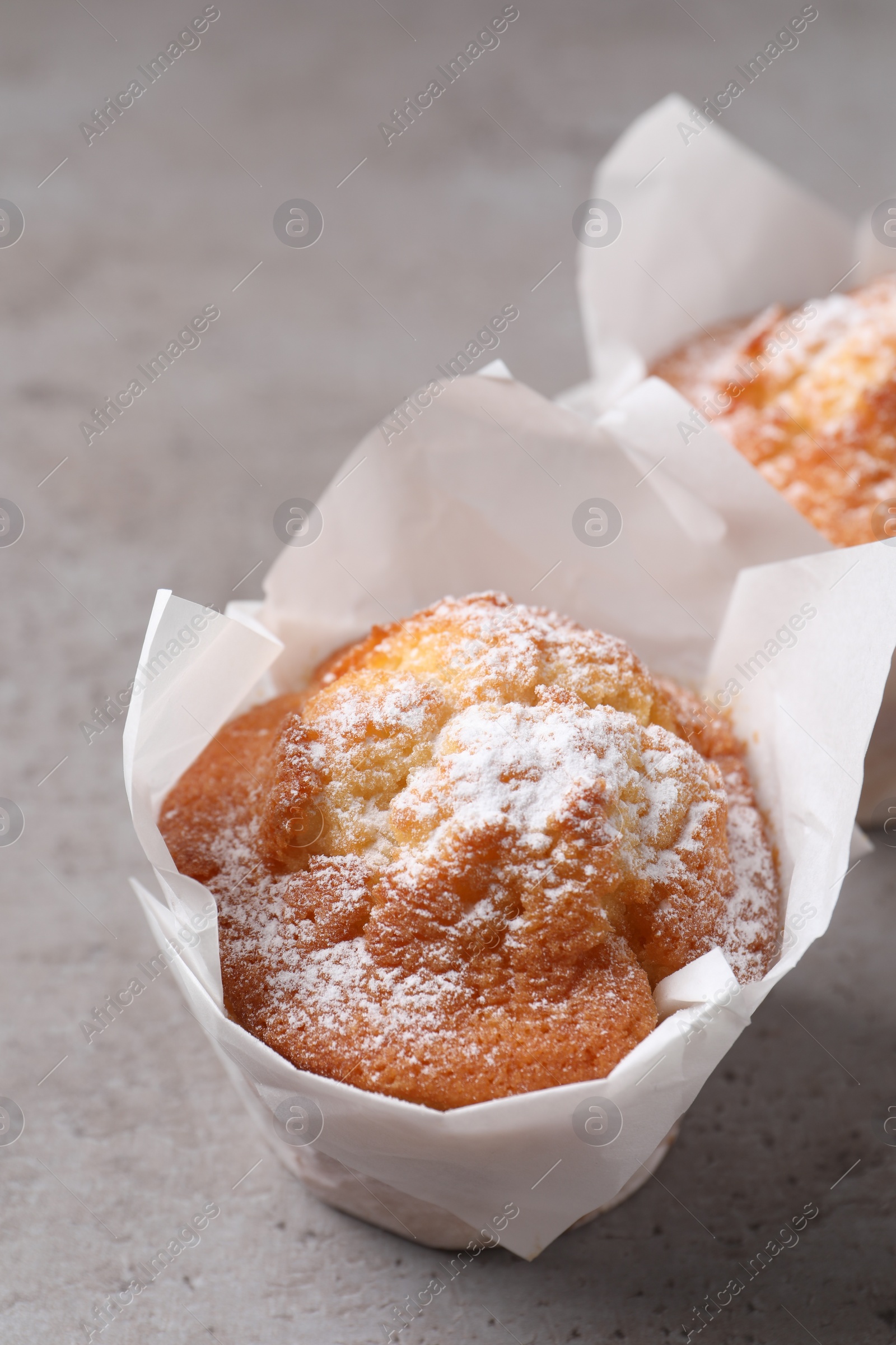 Photo of Delicious muffins with powdered sugar on grey table, closeup