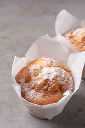 Delicious muffins with powdered sugar on grey table, closeup