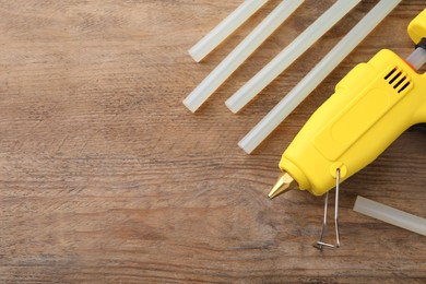 Photo of Yellow glue gun and sticks on wooden table, flat lay. Space for text