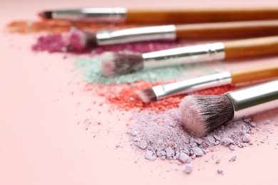 Photo of Different makeup brushes with crushed cosmetic products on pink background, closeup. Space for text