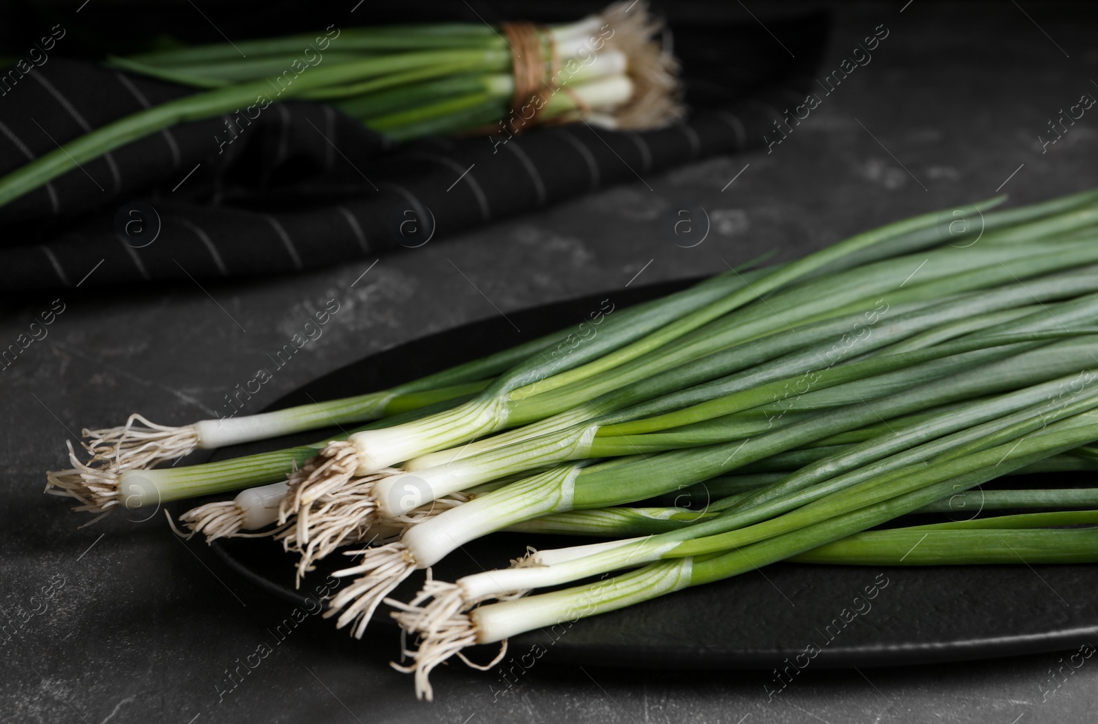 Photo of Fresh green spring onions on slate board, closeup