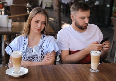 Photo of Young man with smartphone ignoring his girlfriend in outdoor cafe. Boring date