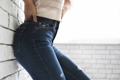 Woman wearing jeans near brick wall indoors, closeup