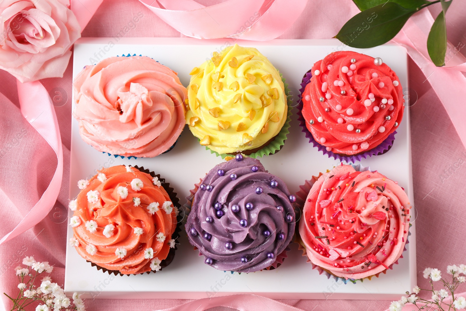 Photo of Delicious cupcake with bright cream on pink fabric, top view