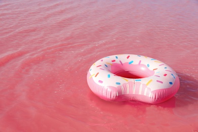 Photo of Bright inflatable ring floating in pink lake on summer day