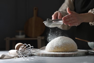 Photo of Making dough. Woman sifting flour at grey table, closeup