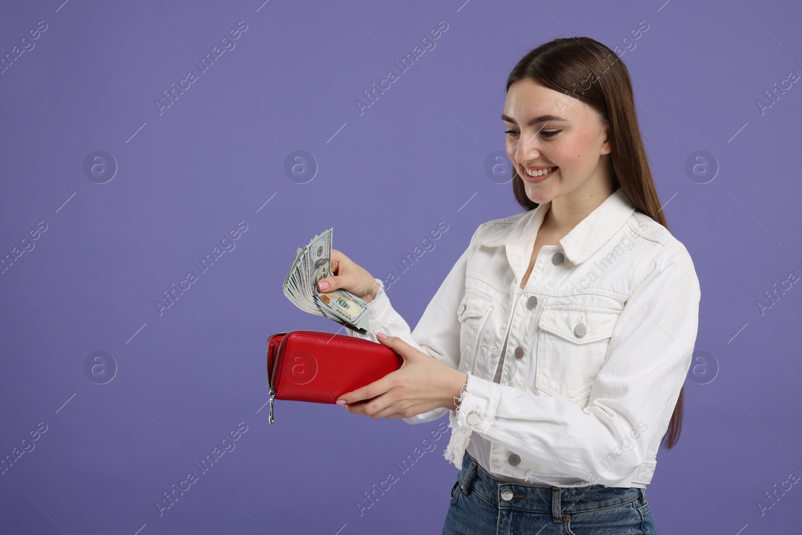 Photo of Happy woman putting money into wallet on purple background, space for text