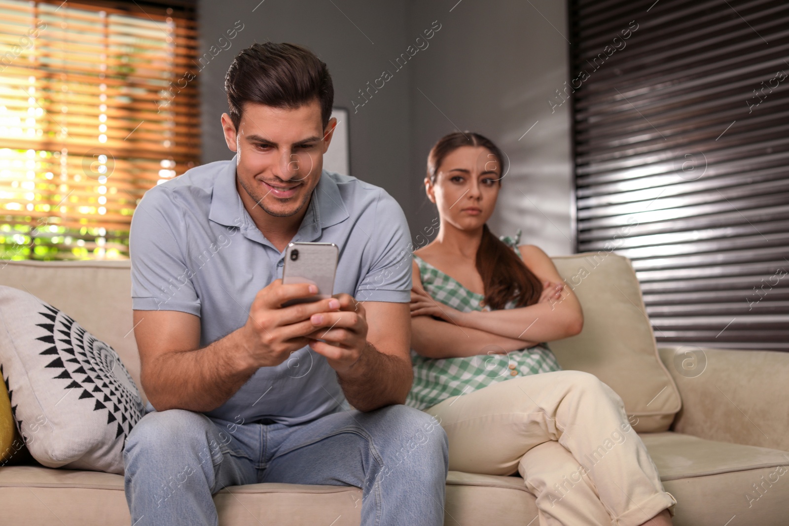 Photo of Man preferring smartphone over spending time with his girlfriend at home. Jealousy in relationship