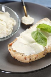 Photo of Piece of bread with cream cheese and basil leaves on table, closeup