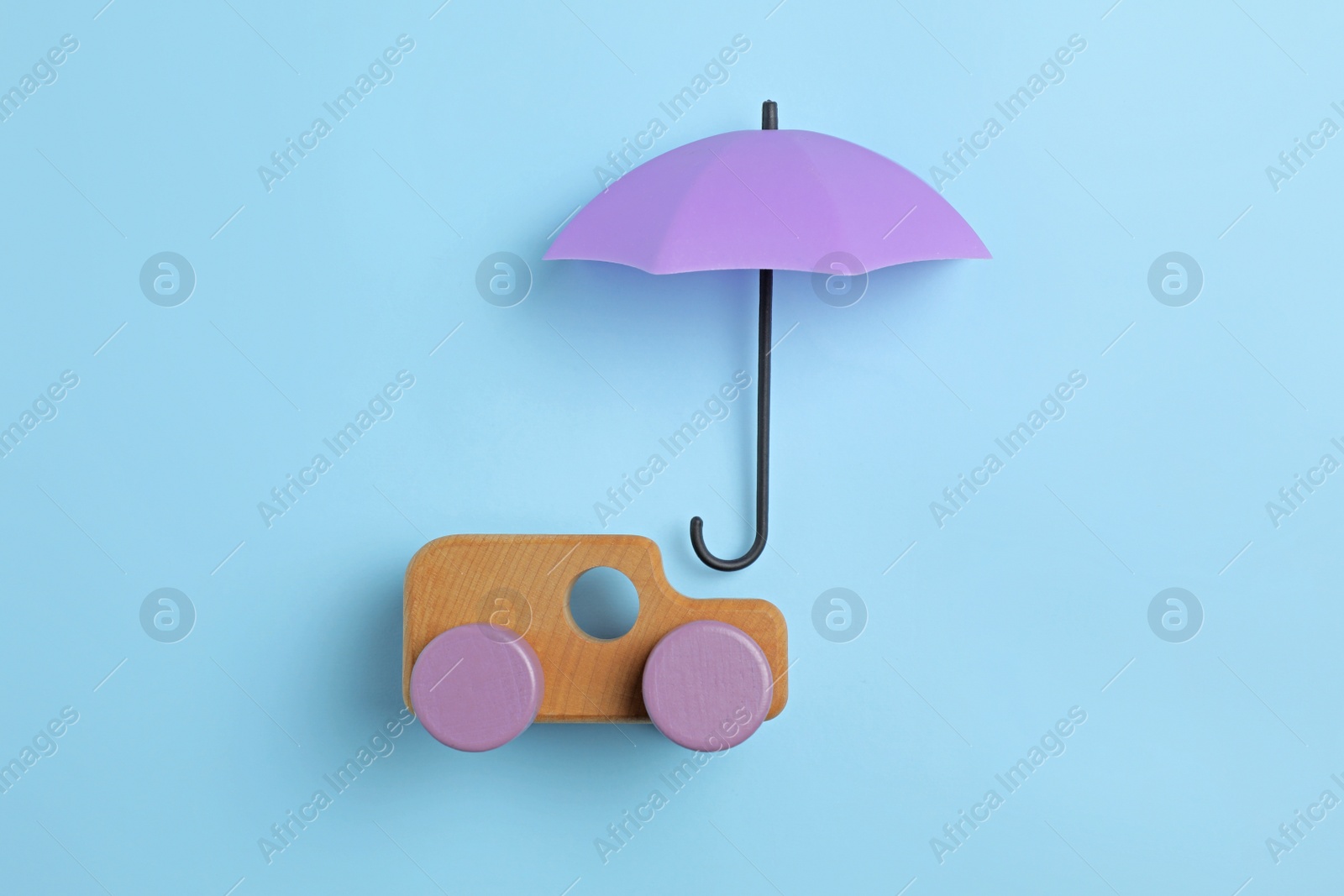 Photo of Bright umbrella and toy car on light blue background, flat lay