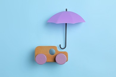 Bright umbrella and toy car on light blue background, flat lay