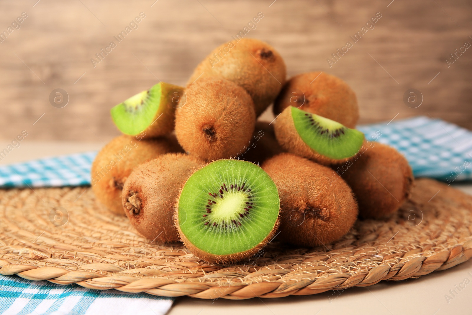 Photo of Heap of whole and cut fresh kiwis on wicker mat