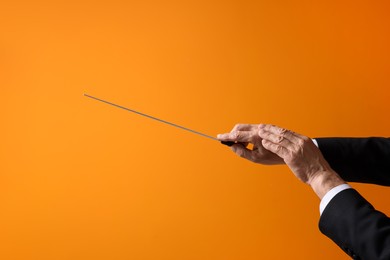 Professional conductor with baton on orange background, closeup. Space for text