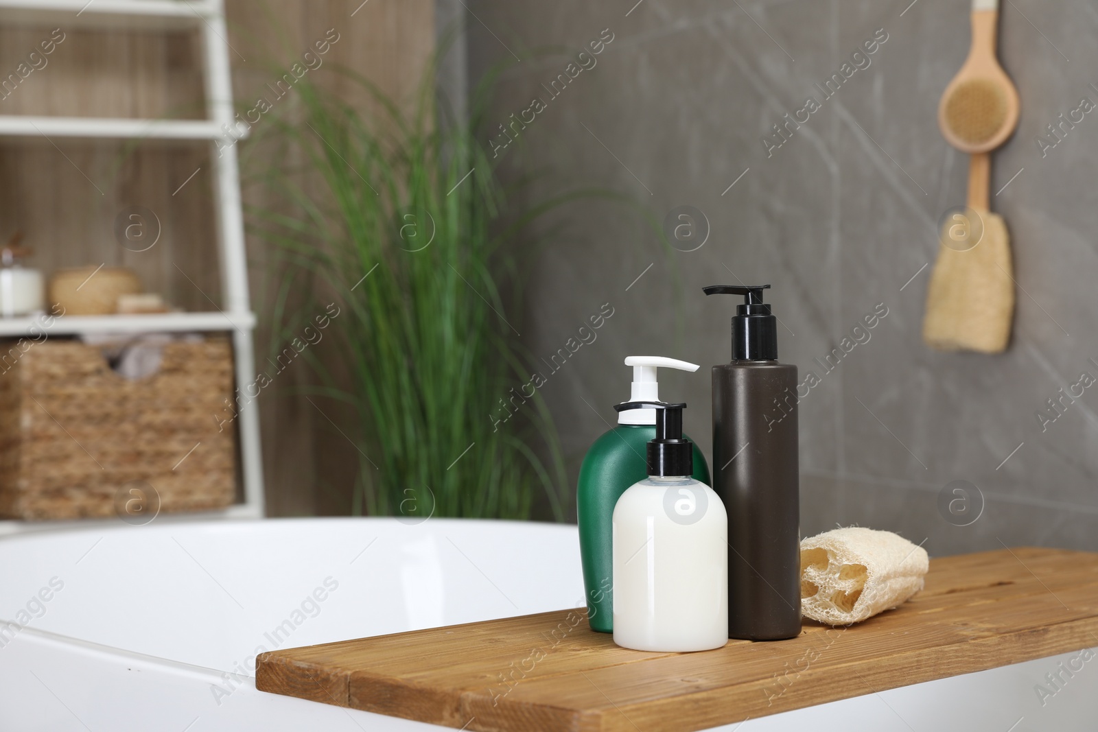 Photo of Wooden bath tray with bottles of shower gels and loofah on tub indoors, space for text
