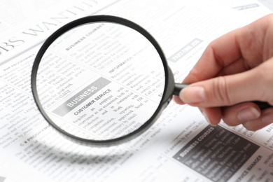 Woman looking through magnifying glass at newspaper, closeup. Job search concept