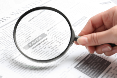 Photo of Woman looking through magnifying glass at newspaper, closeup. Job search concept