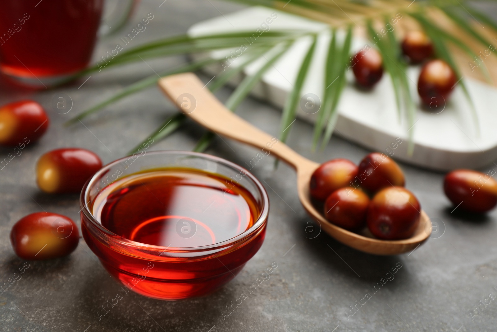 Photo of Palm oil in glass bowl, tropical leaf and fruits on grey table. Space for text