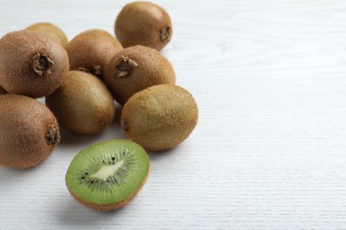Photo of Cut and whole fresh kiwis on white wooden table, space for text