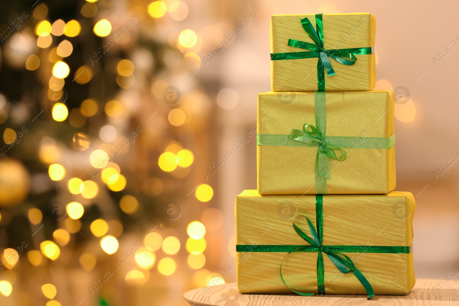 Photo of Beautifully wrapped gift boxes on wooden table against blurred festive lights, space for text. Christmas celebration