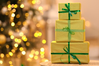 Photo of Beautifully wrapped gift boxes on wooden table against blurred festive lights, space for text. Christmas celebration