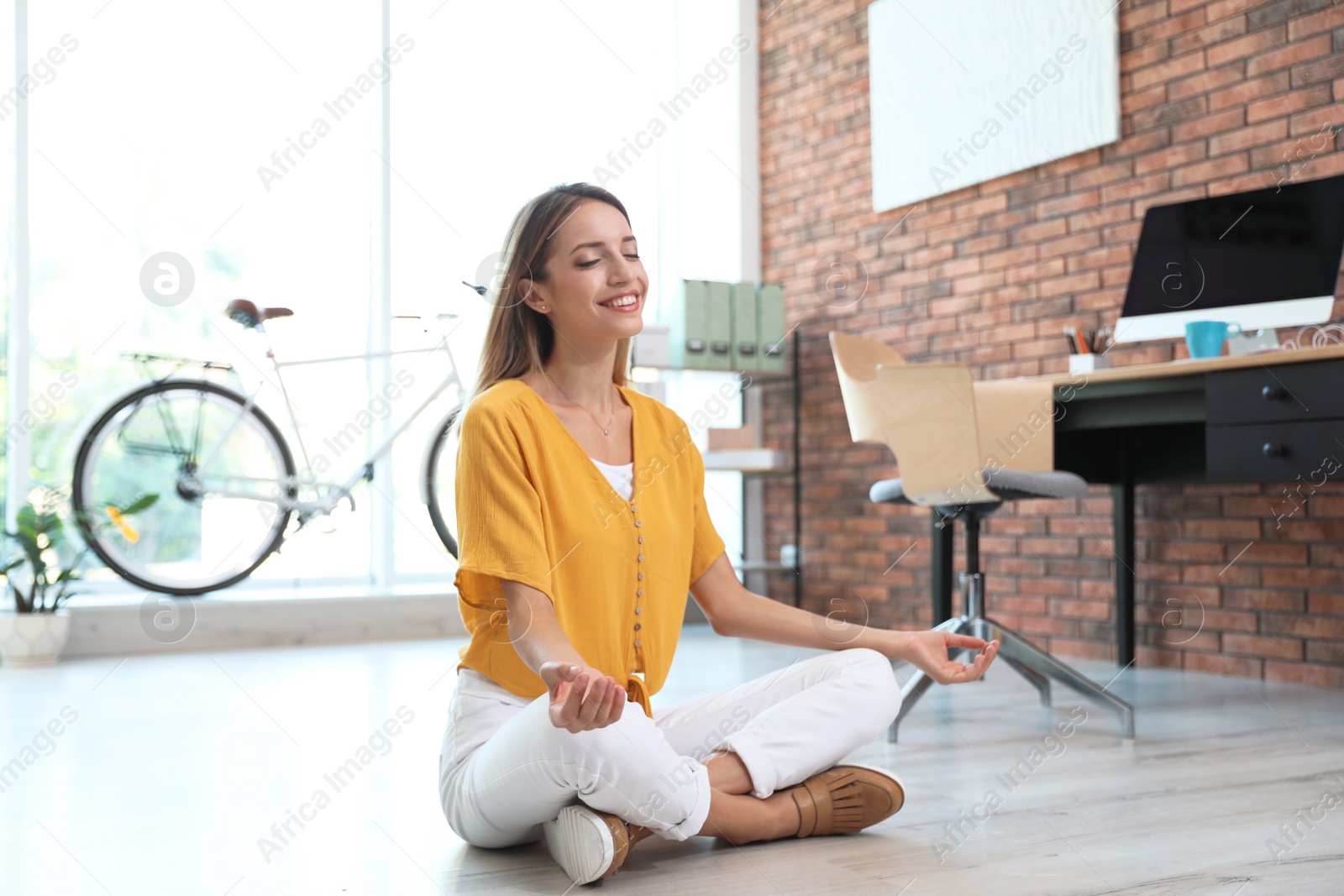 Photo of Beautiful young businesswoman doing yoga in office. Workplace fitness