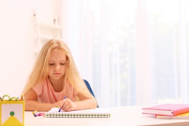 Upset little left-handed girl drawing at table in room