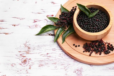 Photo of Tasty elderberries (Sambucus) on white wooden table, space for text