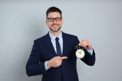 Photo of Happy businessman pointing on alarm clock against grey background. Time management