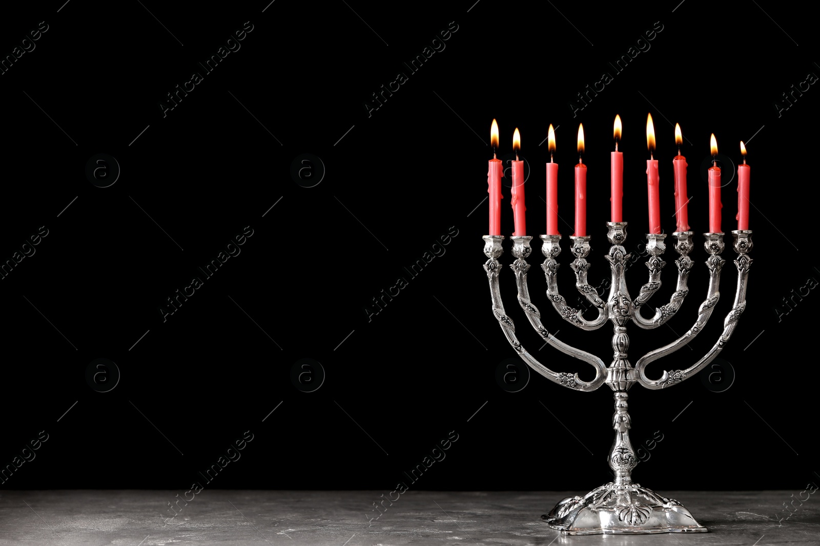 Photo of Silver menorah with burning candles on table against black background, space for text. Hanukkah celebration