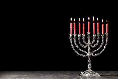 Photo of Silver menorah with burning candles on table against black background, space for text. Hanukkah celebration