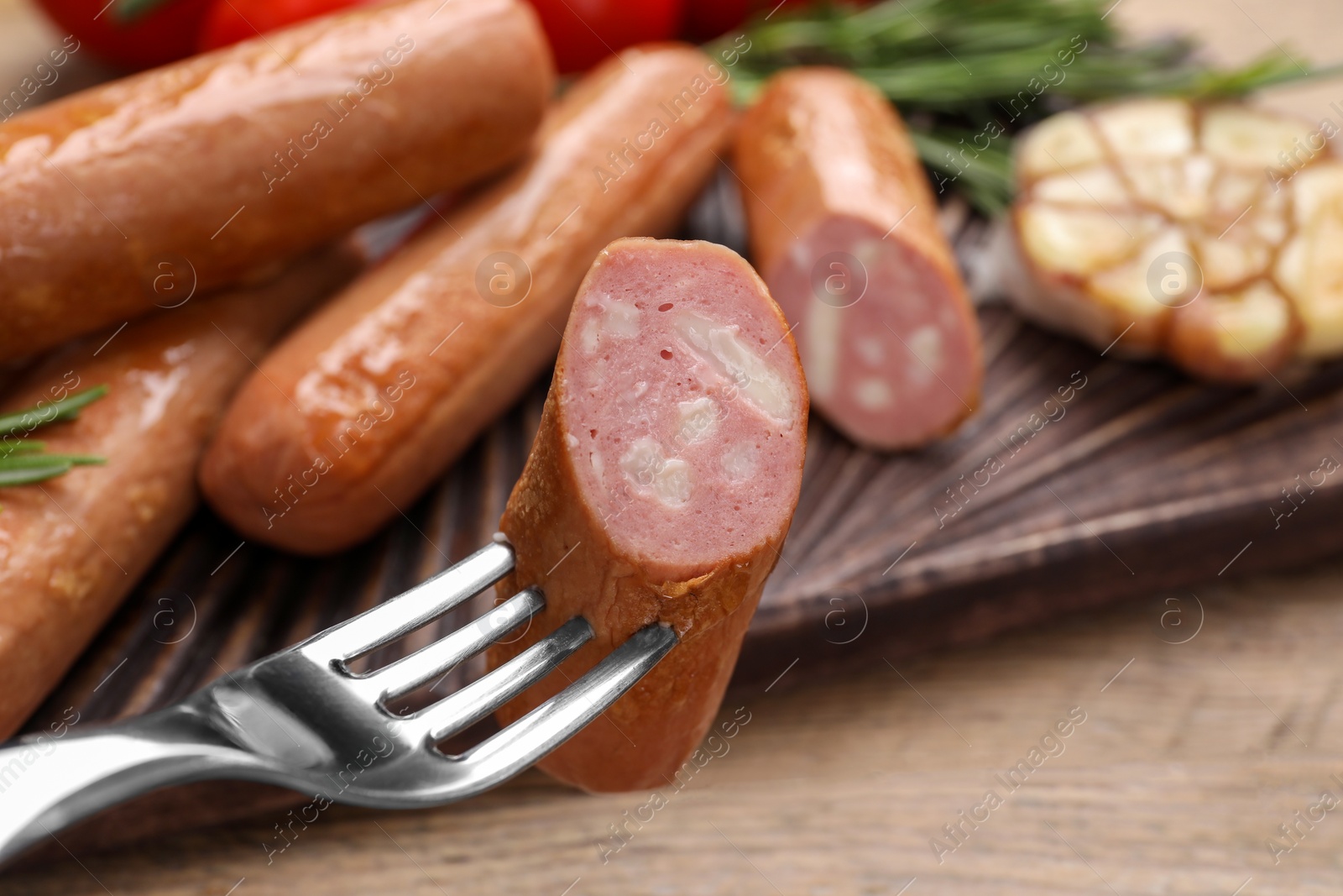 Photo of Delicious vegan sausage on fork over wooden table, closeup