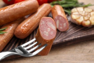 Photo of Delicious vegan sausage on fork over wooden table, closeup