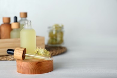 Photo of Bottle of essential oil and linden flowers on white wooden table. Space for text