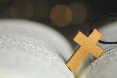 Photo of Christian cross on open Bible against blurred background, closeup