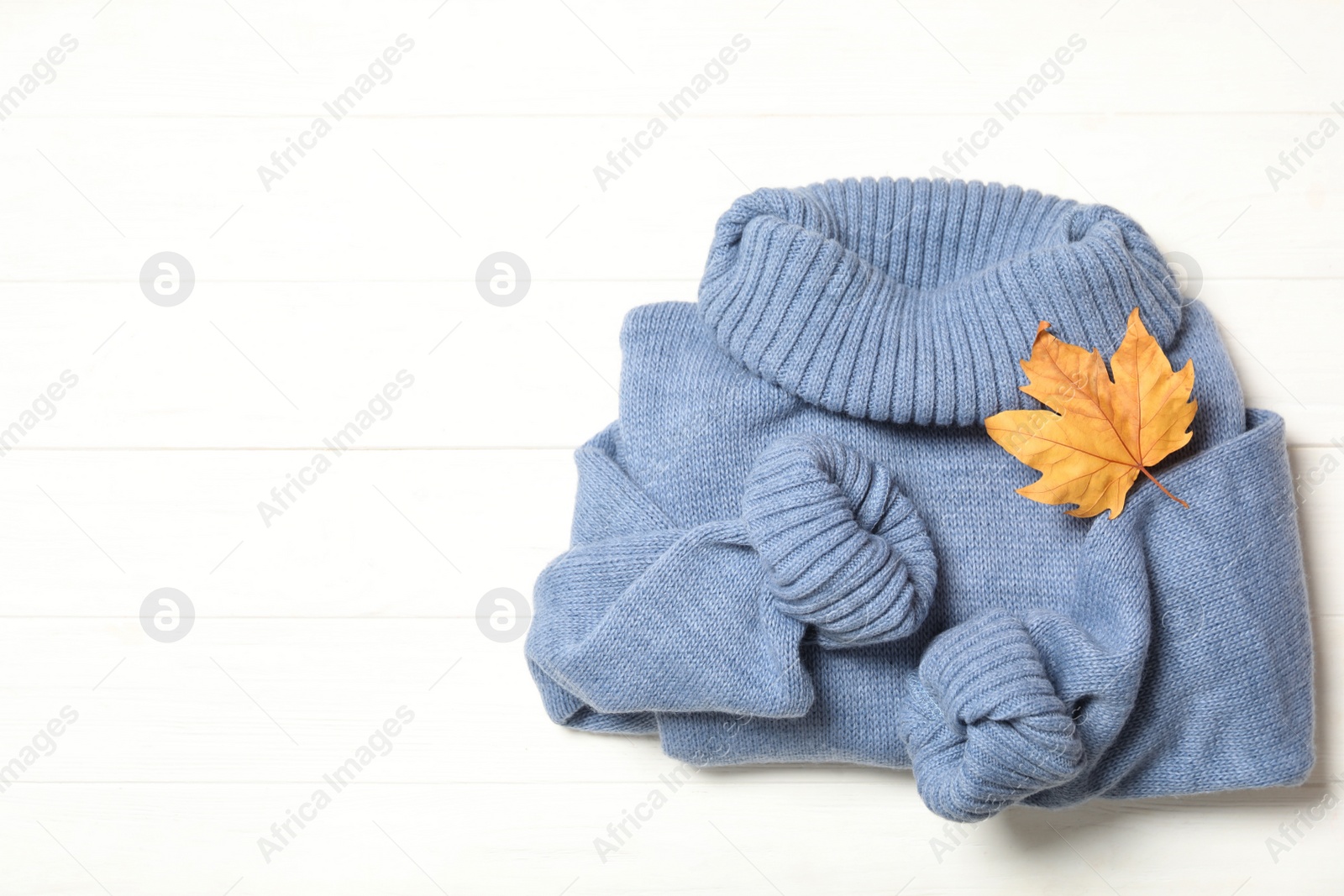 Photo of Top view of warm sweater and dry leaf on white wooden background, space for text. Autumn season