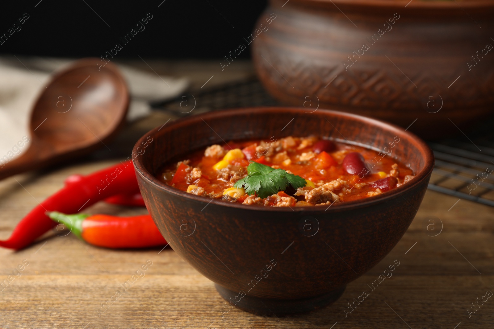 Photo of Bowl with tasty chili con carne on wooden table, closeup