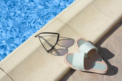 Stylish sunglasses and slippers at poolside on sunny day. Beach accessories