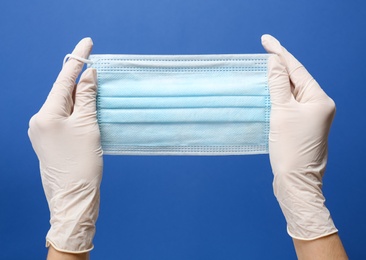 Photo of Doctor holding medical mask on blue background, closeup