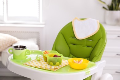 Photo of High chair with food in baby tableware on tray indoors