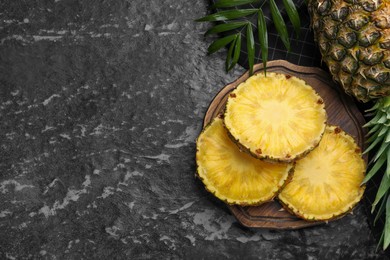 Photo of Slices of tasty ripe pineapple on black textured table, flat lay. Space for text