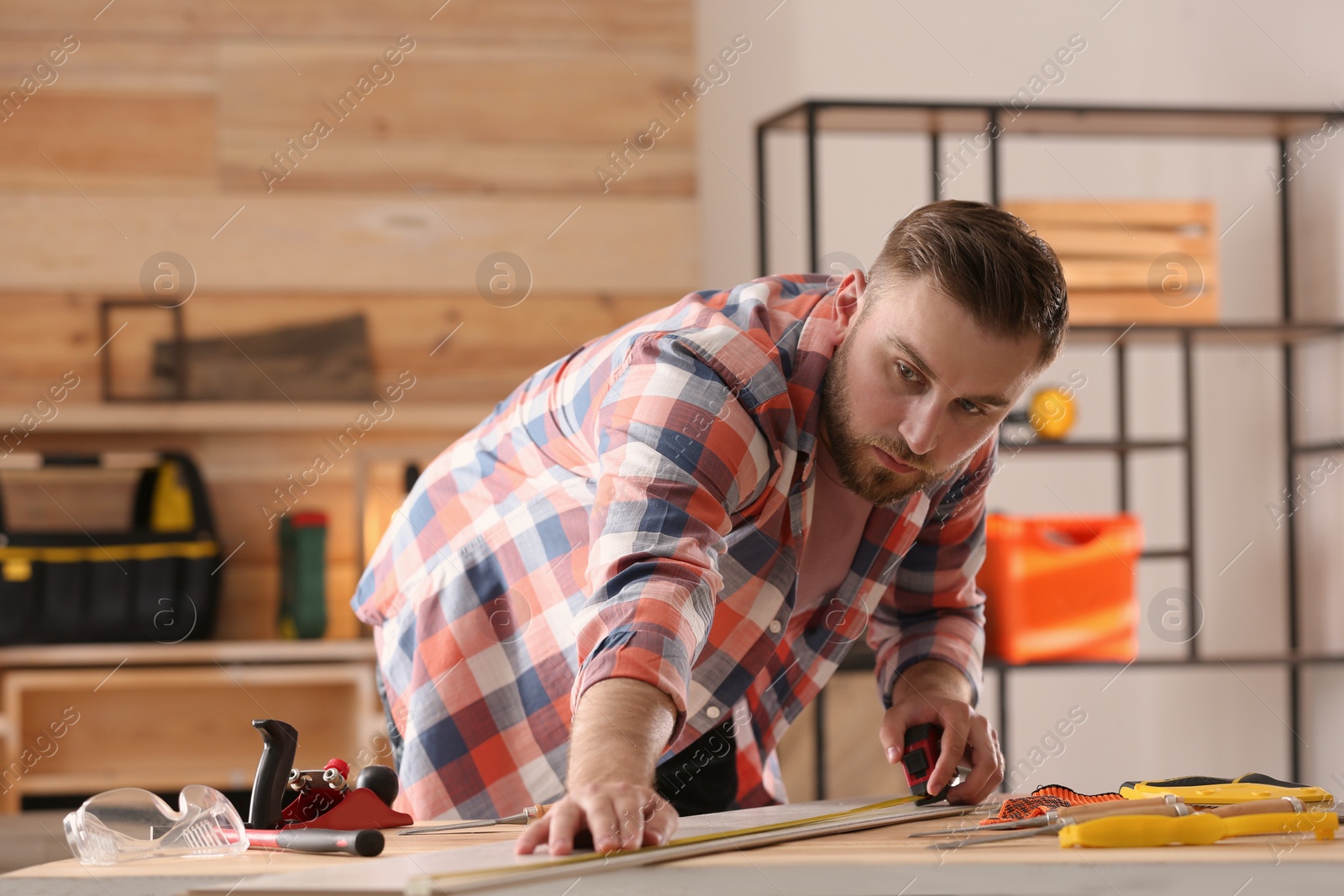 Photo of Carpenter measuring wooden plank at table in workshop