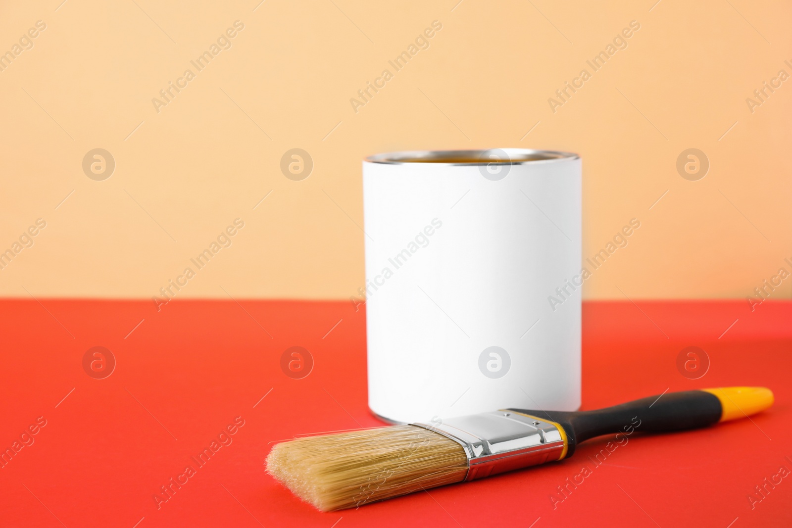 Photo of Blank can of paint with brush on table against color background