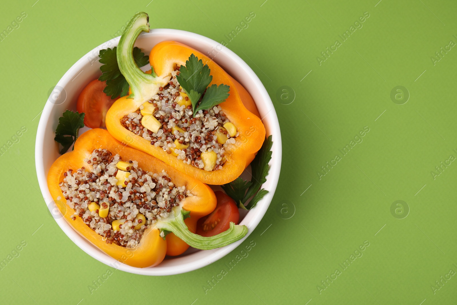 Photo of Quinoa stuffed bell pepper and parsley in bowl on green background, top view. Space for text