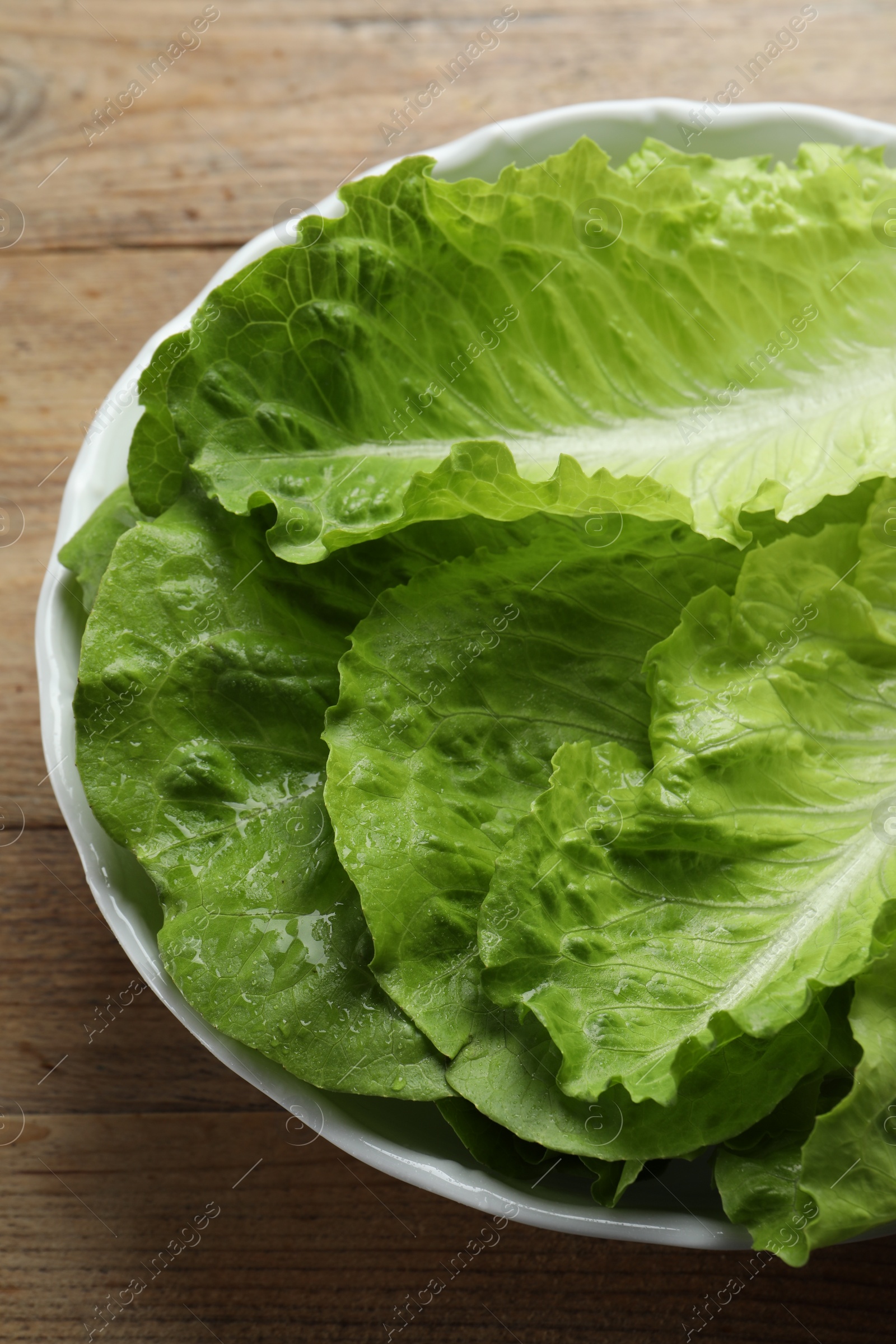 Photo of Bowl with fresh leaves of green romaine lettuce on wooden table, above view