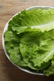 Photo of Bowl with fresh leaves of green romaine lettuce on wooden table, above view
