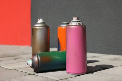 Photo of Cans of different spray paints on pavement near wall, closeup
